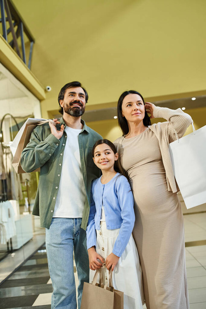 Una famiglia trasporta felicemente le borse della spesa mentre passeggia attraverso un vivace centro commerciale in una gita di fine settimana. - Foto, immagini