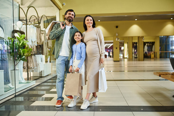 Egy terhes nő és kislánya kényelmesen sétálnak egy nyüzsgő bevásárlóközpontban, különleges pillanatokat osztanak meg egymással.. - Fotó, kép