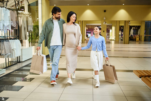 Alışveriş torbaları taşıyan mutlu bir aile, hafta sonu gezintisi için kalabalık bir alışveriş merkezinde rahatça dolaşır.. - Fotoğraf, Görsel