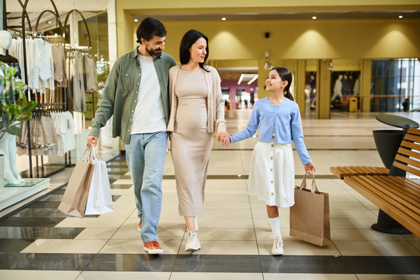 Щаслива сім'я проходить через зайнятий торговельний центр, несучи торговельні пакети, повні покупок. - Фото, зображення