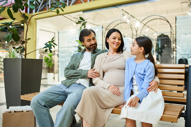 Une famille joyeuse profite d'une journée shopping, assise ensemble sur un banc dans un centre commercial animé. - Photo, image