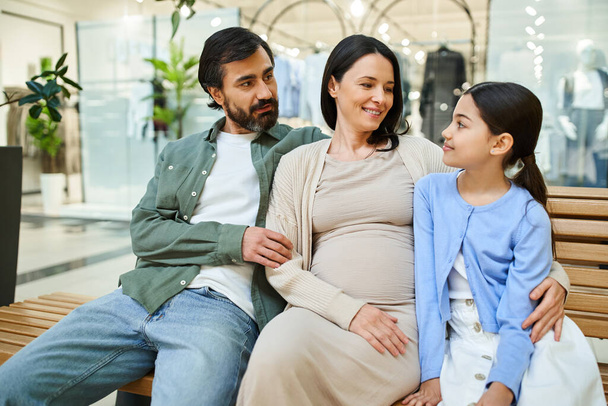 妊娠中の女性と娘がベンチに座り,モールでショッピング週末を楽しんでいます.. - 写真・画像