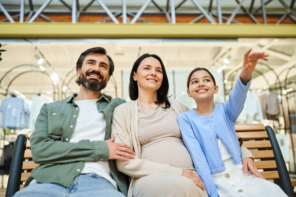 Uma família alegre com crianças sentadas juntas em um banco em um shopping center movimentado, fazendo uma pausa das compras. - Foto, Imagem