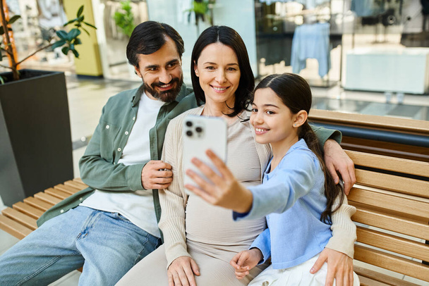 Eine quirlige Familie genießt ein Shopping-Wochenende, sitzt auf einer Bank in einem Einkaufszentrum und macht gemeinsam ein fröhliches Selfie. - Foto, Bild