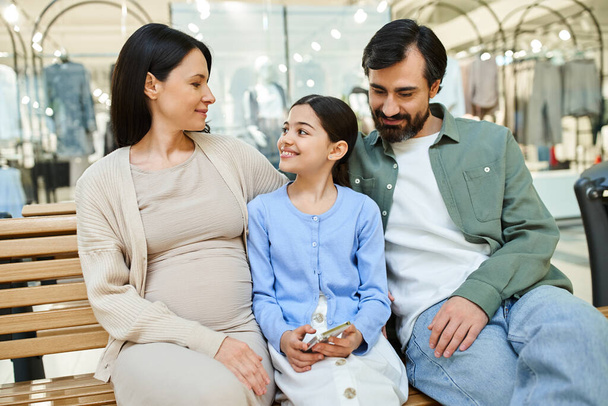 Uma mulher grávida e sua filha compartilham um momento terno em um banco em um movimentado shopping. - Foto, Imagem