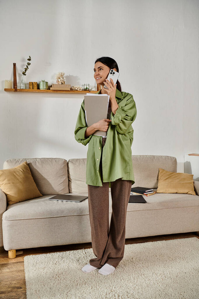 Egy alkalmi ruhás nő áll egy hangulatos nappaliban, akit elnyelt egy telefonhívás.. - Fotó, kép