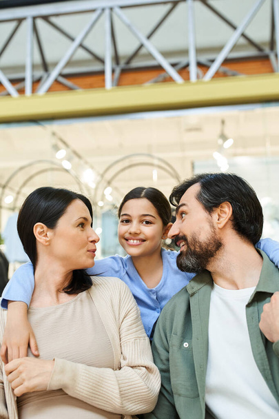 Μια ευτυχισμένη οικογένεια μοιράζεται μια στιγμή σύνδεσης, κοιτάζοντας ο ένας τον άλλο στοργικά κατά τη διάρκεια των αγορών τους στο εμπορικό κέντρο. - Φωτογραφία, εικόνα