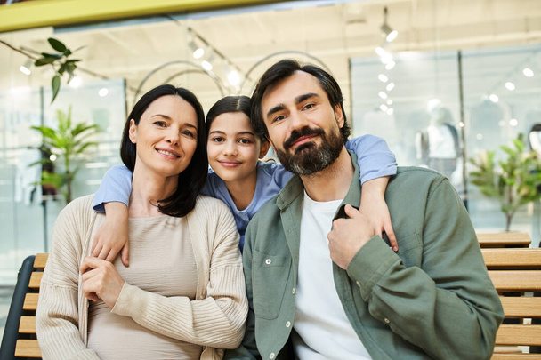 Μια χαρούμενη οικογένεια κάνει ένα διάλειμμα σε ένα παγκάκι απολαμβάνοντας μια εκδρομή για ψώνια μαζί σε ένα κατάστημα. - Φωτογραφία, εικόνα