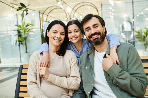 Μια χαρούμενη οικογένεια κάθεται σε ένα παγκάκι σε ένα ζωντανό εμπορικό κέντρο, απολαμβάνοντας μια κοινή στιγμή εν μέσω εκδρομή το Σαββατοκύριακο τους. - Φωτογραφία, εικόνα