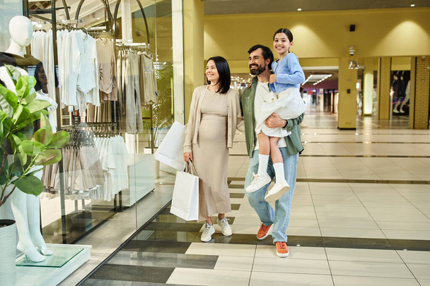 A happy family, parents and kid, leisurely walk through a bustling shopping mall on a weekend outing. - Photo, Image