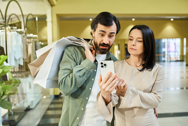 Een man en vrouw verzonken in een mobiele telefoon in een bruisend winkelcentrum. - Foto, afbeelding