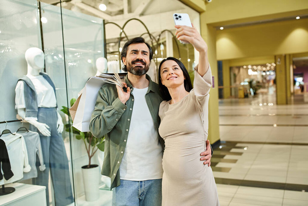 Een vrolijk stel, midden in een bruisend winkelcentrum, omarmt voor een selfie, vangt hun gedeelde geluksmomenten op. - Foto, afbeelding