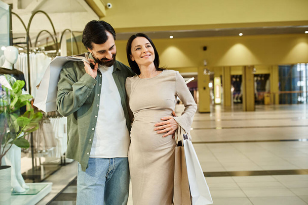 Egy terhes nő és egy férfi kényelmesen sétálhat át egy vibráló bevásárlóközponton egy pihentető hétvégi napon. - Fotó, kép
