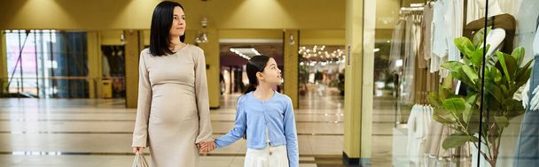Eine Frau und ein Kind spazieren fröhlich durch ein belebtes Einkaufszentrum und teilen einen verbindenden Moment inmitten des Einkaufstrubels. - Foto, Bild