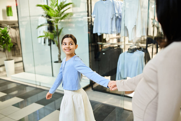 A woman and a young girl happily shop for clothes together in a bustling store. - Photo, Image