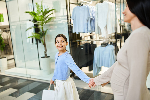 Uma alegre mãe e filha caminham de mãos dadas em um animado shopping center, desfrutando de uma divertida excursão em família. - Foto, Imagem