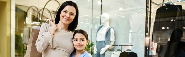 Μια γυναίκα και η κόρη της απολαμβάνουν ένα Σαββατοκύριακο για ψώνια μαζί, εξερευνώντας ένα πολυσύχναστο εμπορικό κέντρο με χαμόγελα στα πρόσωπά τους. - Φωτογραφία, εικόνα