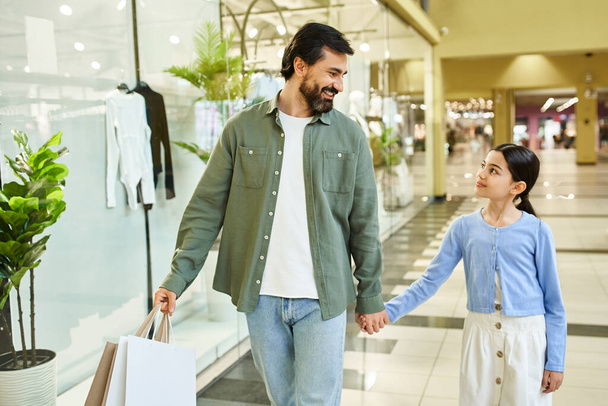 Un homme et une fille marchent joyeusement dans un centre commercial, tenant des sacs remplis d'achats. - Photo, image