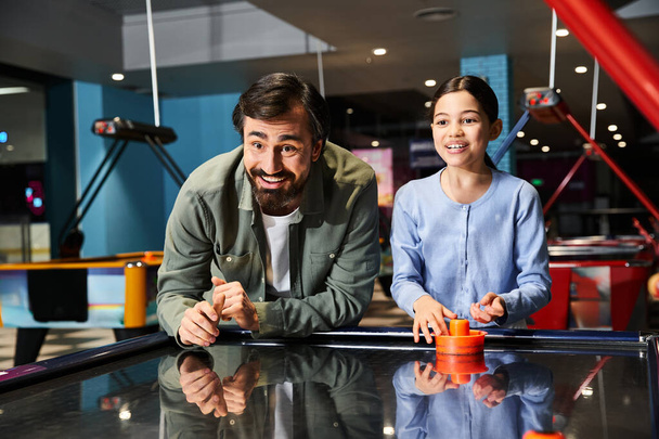 A dad and daughter engage in an intense game of air hockey at a gaming zone in a mall, having a fun family weekend. - Photo, Image