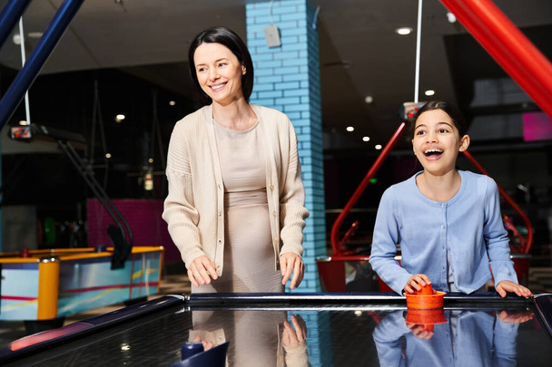 Eine Mutter und ihre Tochter spielen fröhlich Airhockey in einer Spielhalle während eines lustigen Wochenendausflugs im Einkaufszentrum. - Foto, Bild