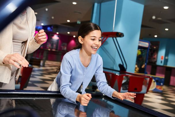 Eine Mutter und ihre Tochter spielen begeistert Airhockey, während sie in einem Einkaufszentrum in Gelächter und Konkurrenzkampf versinken. - Foto, Bild
