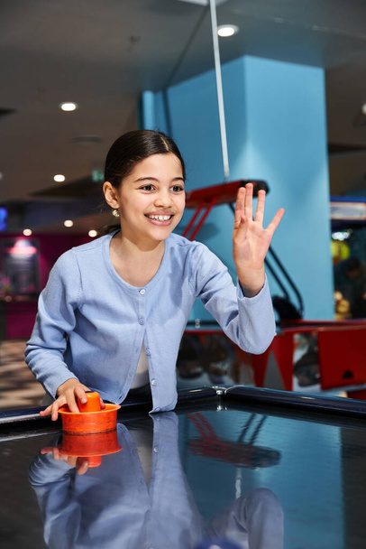 A girl joyfully competes in a game of air hockey with family at a mall gaming zone during the weekend. - Photo, Image