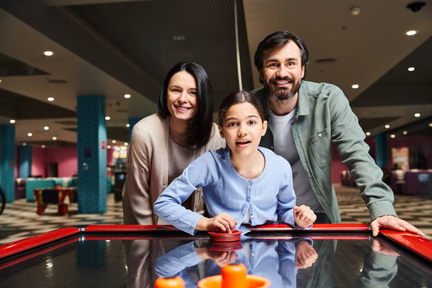 Eine fröhliche Familie, die an einem lebhaften Wochenende in einem geschäftigen Einkaufszentrum begeistert Airhockey spielt. - Foto, Bild