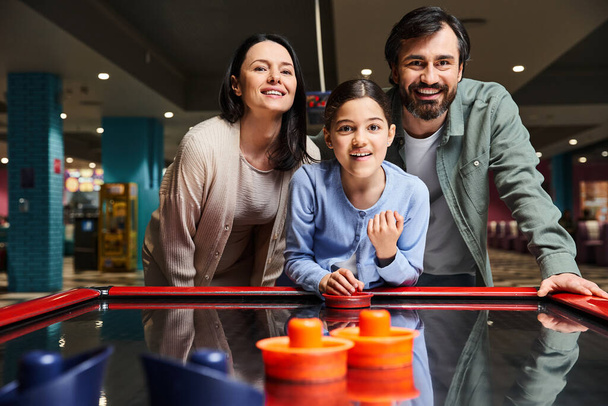 Μια ευτυχισμένη οικογένεια απολαμβάνει ένα παιχνίδι μπιλιάρδου σε ένα arcade κατά τη διάρκεια του Σαββατοκύριακου, γελώντας και ανταγωνίζονται σε ένα φιλικό αγώνα. - Φωτογραφία, εικόνα