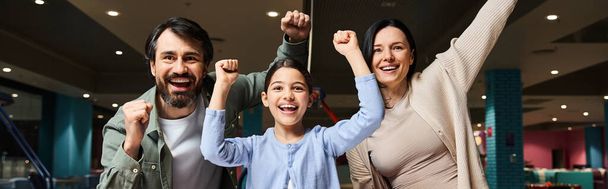 Una famiglia felice alza le braccia in una zona di gioco dei centri commerciali, celebrando l'unità e la felicità durante una gita di fine settimana. - Foto, immagini
