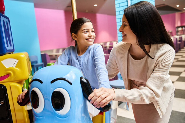 Eine Frau und ein Kind lachen, als sie am Wochenende in einem lebhaften Spielwarengeschäft in einem belebten Einkaufszentrum mit einem Spielzeugkarussell spielen. - Foto, Bild