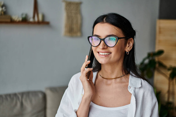 Una donna con gli occhiali parla al cellulare mentre lavora da casa. - Foto, immagini