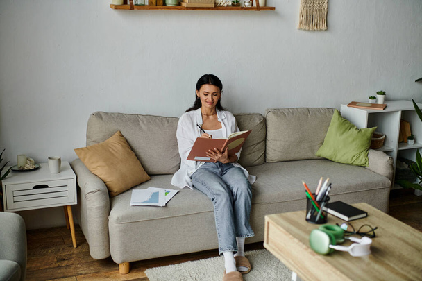 Donna in abbigliamento casual seduta su un divano immersa nella lettura di un libro. - Foto, immagini