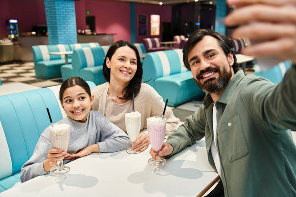 Μια ευτυχισμένη οικογένεια αιχμαλωτίζει μια στιγμή, βγάζοντας μια selfie μαζί σε ένα δείπνο κατά τη διάρκεια μιας εξόρμησης Σαββατοκύριακο. - Φωτογραφία, εικόνα