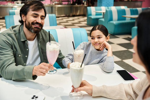 Счастливая семья наслаждается молочными коктейлями в закусочной в выходные дни, смеясь и делясь качеством времени вместе. - Фото, изображение