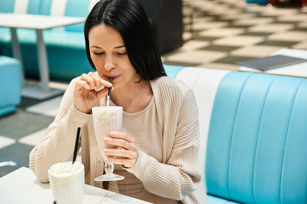 Eine Frau genießt in einem Restaurant einen cremigen Milchshake und genießt den Moment mit einem Lächeln im Gesicht. - Foto, Bild