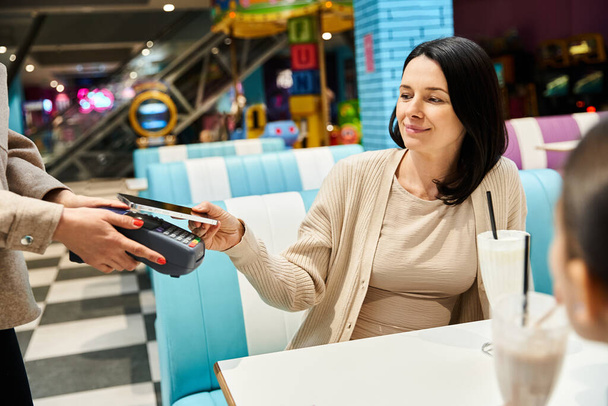 Una mujer le entrega una tarjeta de crédito a una camarera en un restaurante, encarnando un vínculo familiar moderno durante el fin de semana. - Foto, Imagen