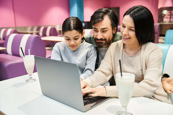 Una famiglia felice di quattro persone siede a un tavolo, impegnata con uno schermo portatile, trascorrendo del tempo insieme in un ambiente moderno. - Foto, immagini