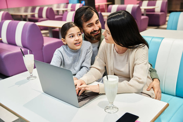 Az örömteli család élvezi a minőségi időt együtt egy étteremben, ahogy összegyűlnek egy laptop körül.. - Fotó, kép