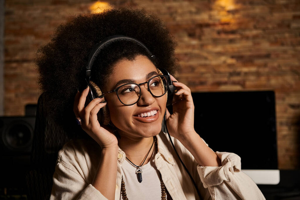 Μια νεαρή γυναίκα που φοράει ακουστικά σε ένα στούντιο ηχογράφησης, βυθισμένη στη μουσική παραγωγή για μια πρόβα μπάντας. - Φωτογραφία, εικόνα