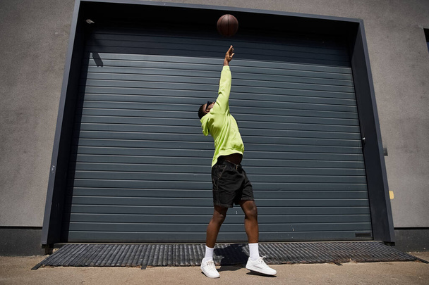 Κομψός Αφροαμερικανός που ντριπλάρει το μπάσκετ μπροστά από το γκαράζ.. - Φωτογραφία, εικόνα