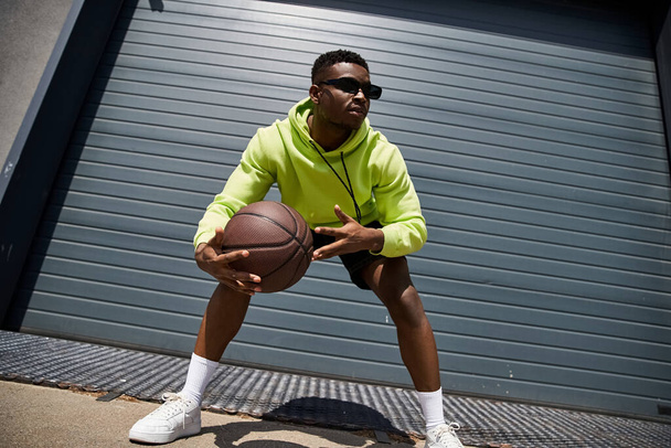 A stylish African American man in a green hoodie holding a basketball. - Photo, Image