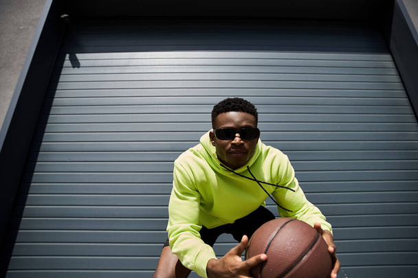 Afro-Amerikaanse man in gele hoodie met basketbal. - Foto, afbeelding