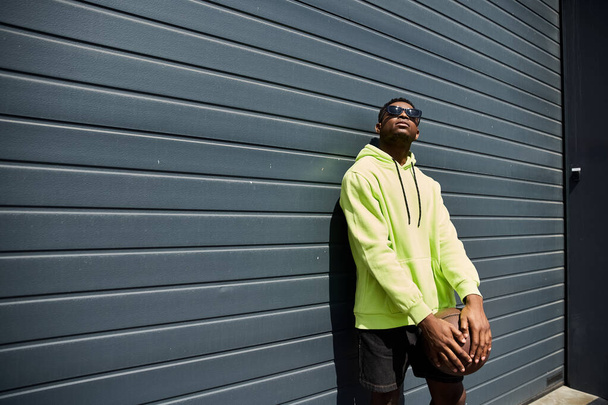 Stylish African American man leans against a wall in a yellow hoodie. - Photo, Image