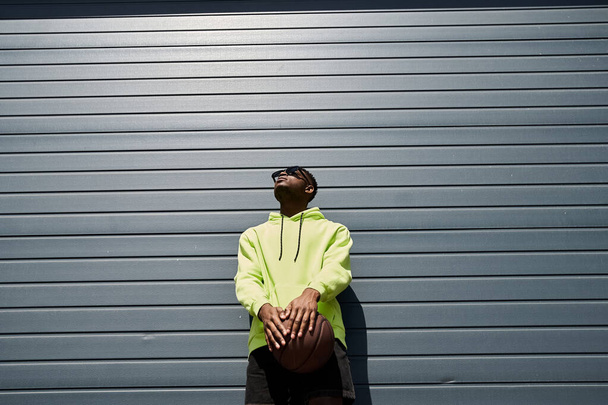 Afrikai amerikai férfi divatos sárga kapucnis gazdaság kosárlabda - Fotó, kép