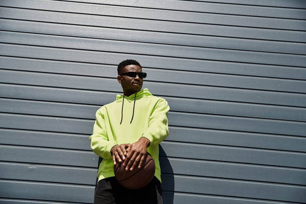 Stylish African American man leans against a wall in a bright neon yellow hoodie. - Photo, Image