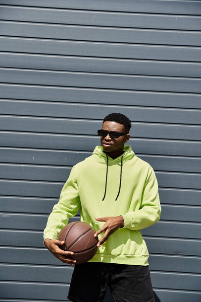 Young African American man in neon green hoodie holds basketball. - Photo, Image