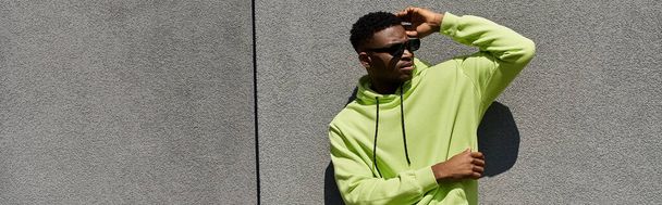 Handsome African American man leaning against wall in stylish green hoodie. - Photo, Image