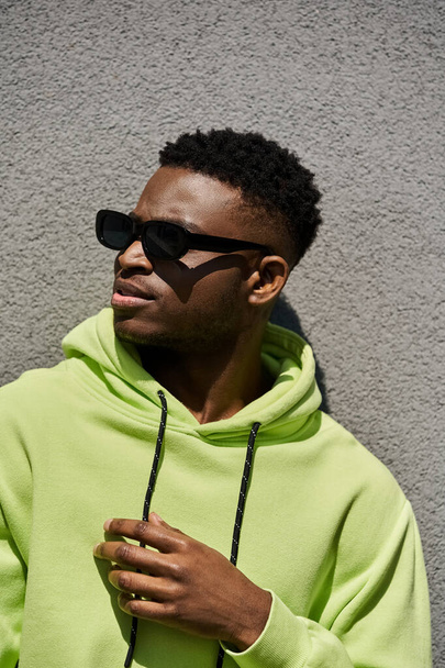 Schöner afroamerikanischer Mann im trendigen lindgrünen Kapuzenpullover und Sonnenbrille. - Foto, Bild