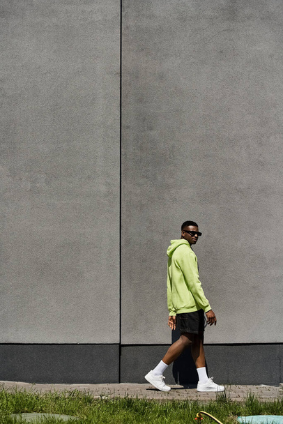 Стильний афроамериканський чоловік в жовтому светрі, що йде сірою стіною. - Фото, зображення