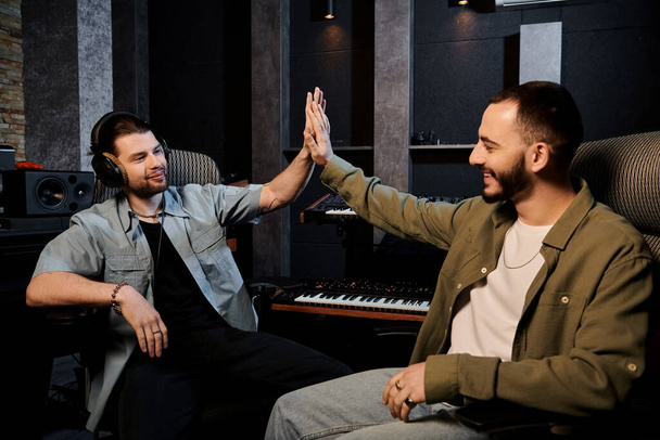 Dois homens em um estúdio de gravação, membros de uma banda de música, comemorando com altos cinco após uma sessão de ensaio bem sucedida. - Foto, Imagem